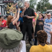 Photo of Father Frank Alagna speaking (with microphone) at a rally in support of Dreamers.