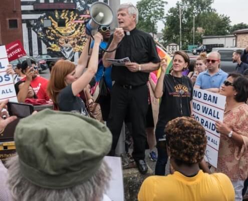 Photo of Father Frank Alagna speaking (with microphone) at a rally in support of Dreamers.