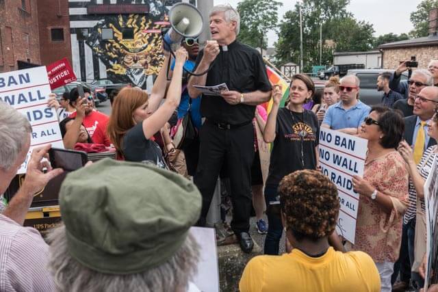 Photo of Father Frank Alagna speaking (with microphone) at a rally in support of Dreamers.