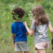 Photo of two children in a meadow, back to the camera, picking flowers.