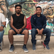 Four Latinos sitting in front of a bright mural.