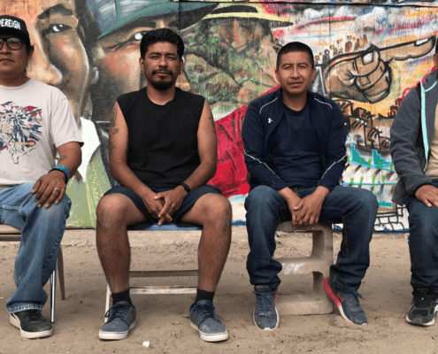 Four Latinos sitting in front of a bright mural.