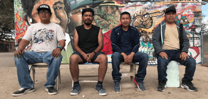 Four Latinos sitting in front of a bright mural.