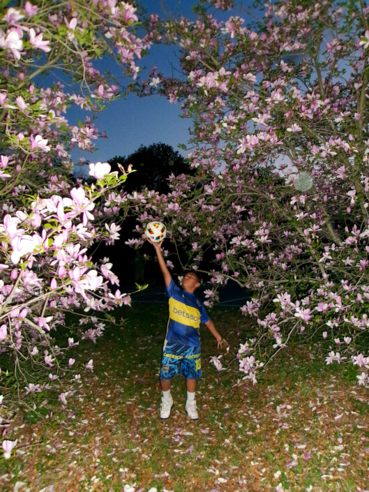 Photo of a kid with soccer ball surrounded by flowering trees.